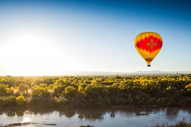 A hot-air balloon over green cottonwoods along the Rio Grande